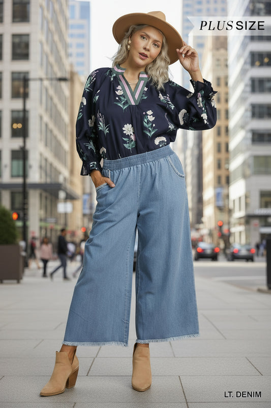 Woman wearing a navy floral blouse and light denim pants on a beige background