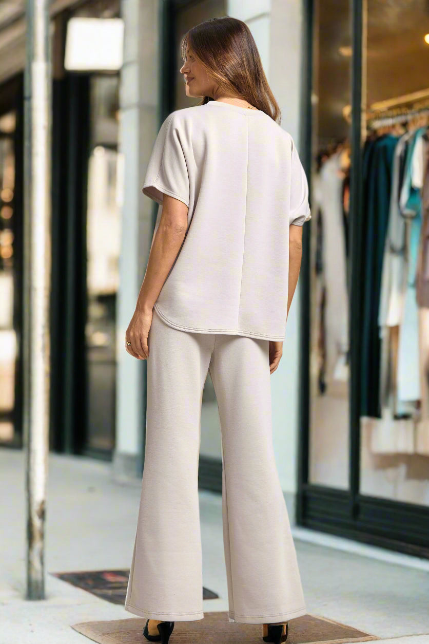 Woman wearing a light-colored outfit with wide-leg pants on a plain background