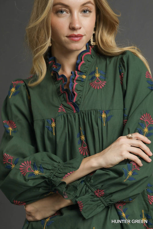 Woman wearing a green embroidered blouse against a gray background